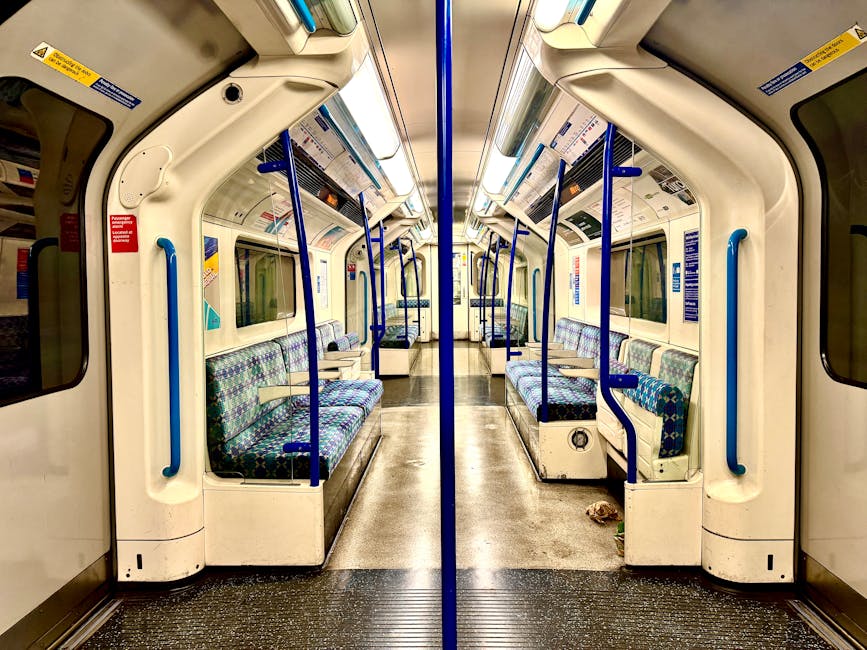 Interior view of a clean, modern train carriage with patterned fabric seats in black, purple, and yellow, arranged along both sides and facing each other. The aisle is clear and free of debris, with a